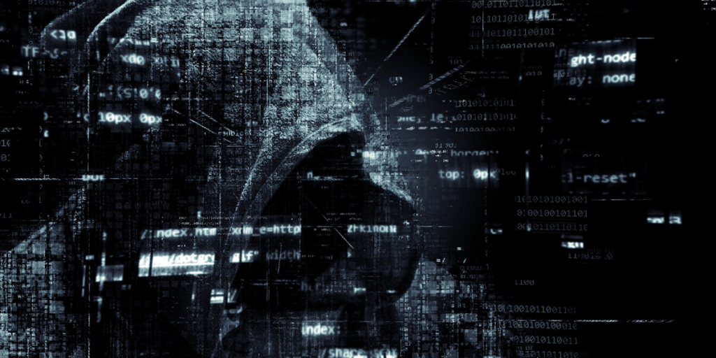 Un hombre con capucha simulando un hacker con código fuente al rededor.