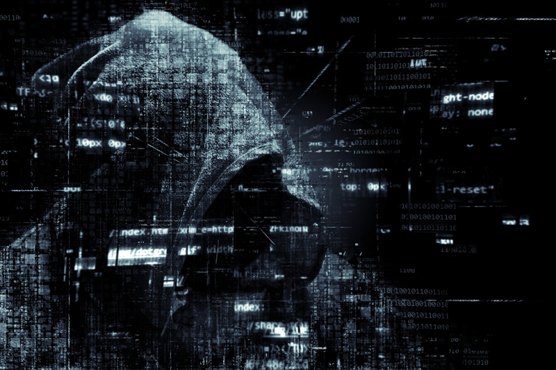 Un hombre con capucha simulando un hacker con código fuente al rededor. 
