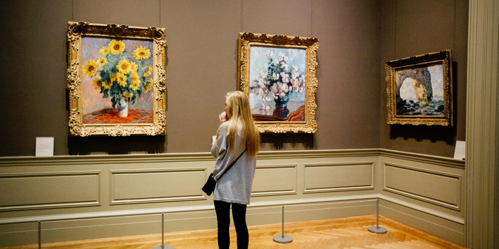 Una chica delante de varios cuadros en el interior de un museo.
