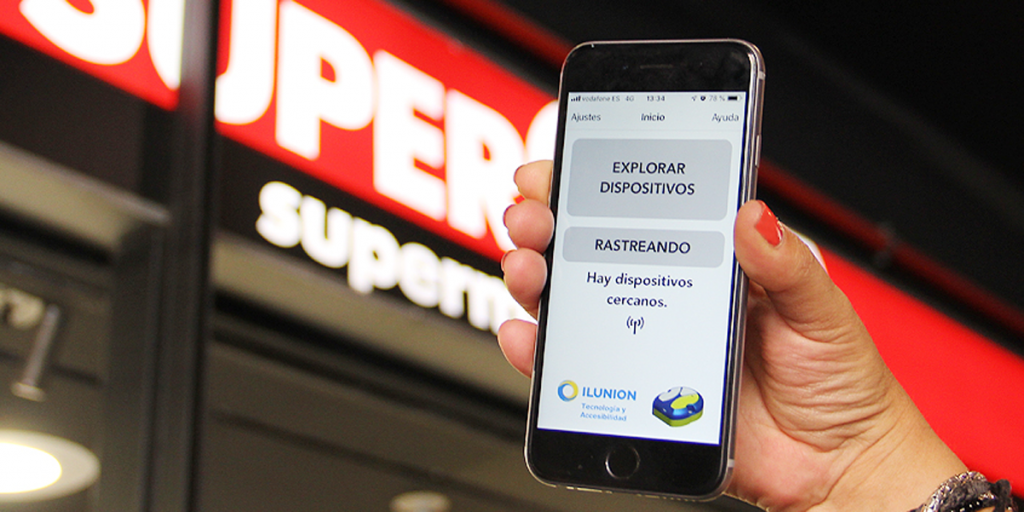 Una mano con un móvil que tiene abierta la aplicación, situada delante de la puerta del supermercado.