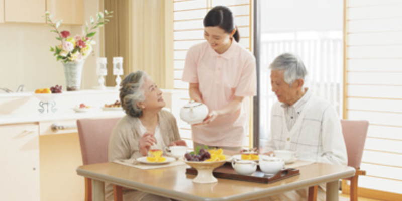Dos ancianos desayunando mientras les ayuda una enfermera.