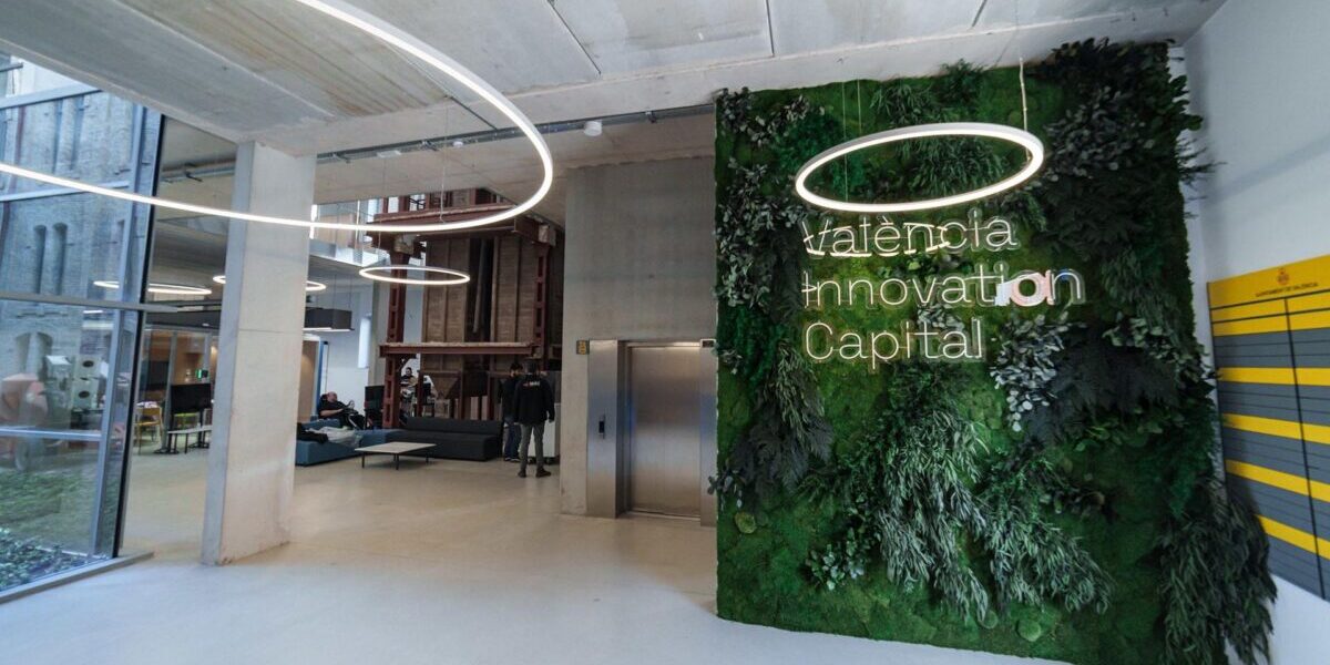 Interior de Les Naus, con un jardín vertical y el rótulo València Innovation Capital junto a la zona de recepción.