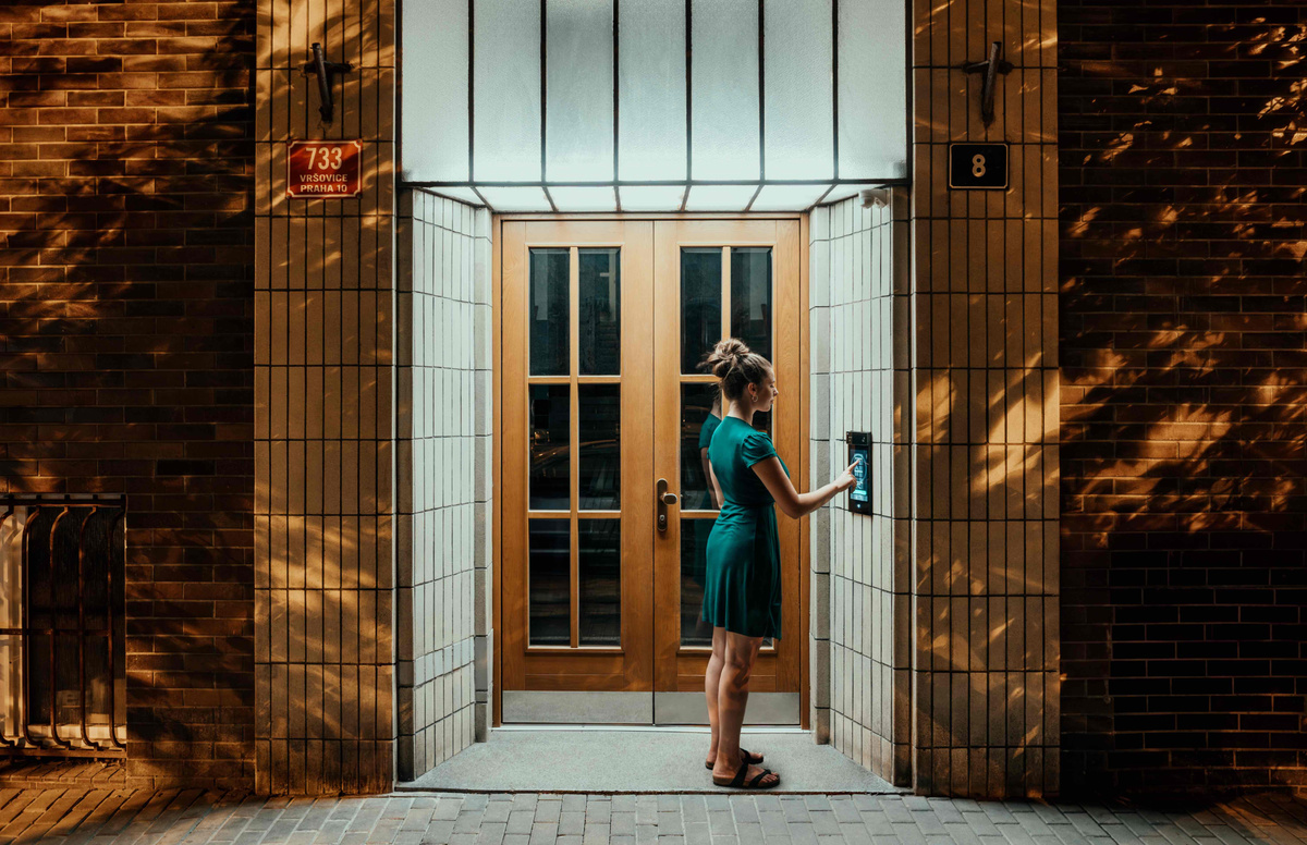 Mujer utilizando un videoportero junto a la puerta de entrada de un edificio residencial.